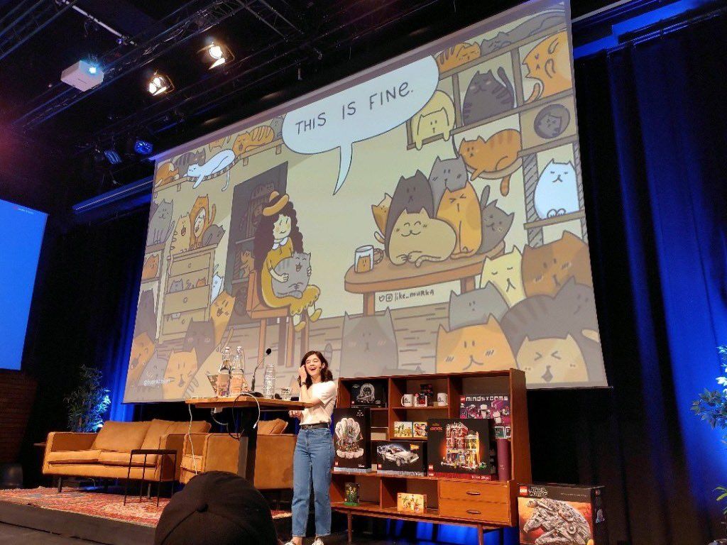 Busra onstage with a drawing of a 'this is fine' cats behind her